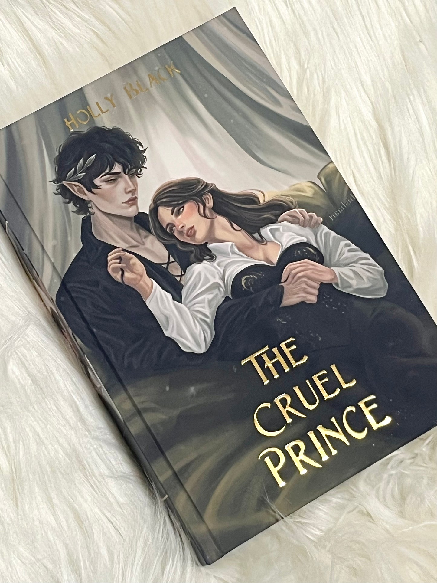Book titled 'The Cruel Prince' with a cover illustration of two characters on a soft white surface.