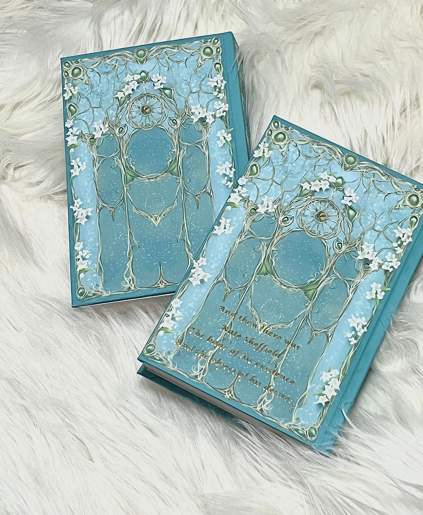 Two decorative blue books with intricate designs on a white fluffy surface